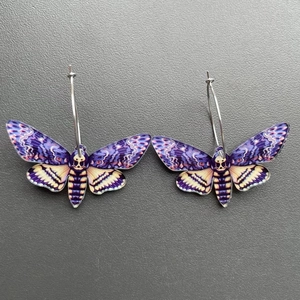 Close-up of acrylic moth earrings with skull pattern and silver rings on grey background