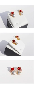 Macro detail of gold earrings featuring red heart gems and white rectangular zircons