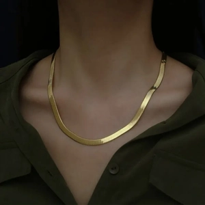 Close-up of golden flat snake bone chain necklace worn on a model's collarbone