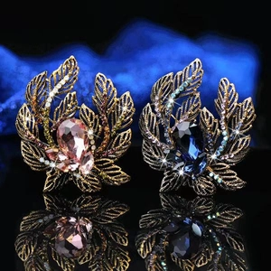 Elegant vintage leaf brooch with pink and blue gemstones on a dark reflective base