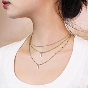 Close-up of triple-layered gold necklace featuring colorful beads and feather pendants