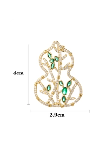 Detailed view of hollow gourd brooch with gold metal, green gems, and crystal accents