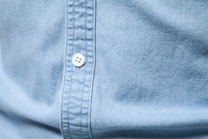 Detail of white button and stitching on light blue cotton denim shirt fabric