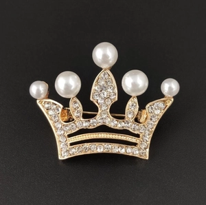 Detail of gold crown brooch with white pearls and sparkling rhinestones on black background