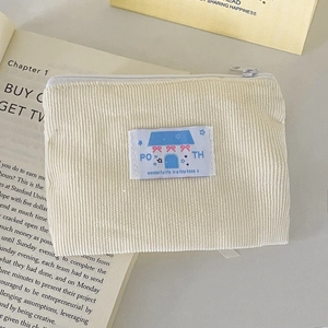 Dettaglio ravvicinato della pochette in velluto a coste crema con patch a fiocco