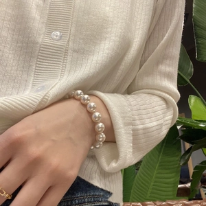 Close-up of elegant white pearl elastic bracelet worn with a casual knitted cardigan