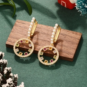 Elegant gold earrings with colorful zircon stones and pearls on a festive wood stand