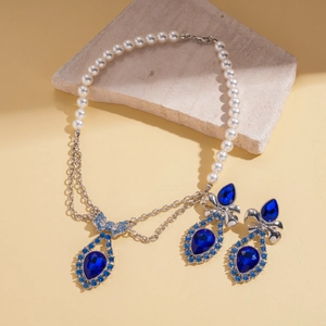 Detail view of pearl and chain necklace with blue teardrop gems and diamond bows