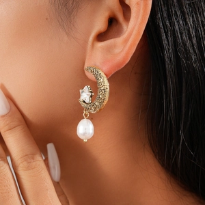 Close-up of vintage gold moon and star earrings with white pearl pendant on model