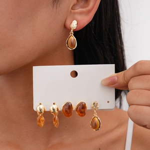 Detail view of gold-tone earrings set with amber resin drop and oval shapes on model