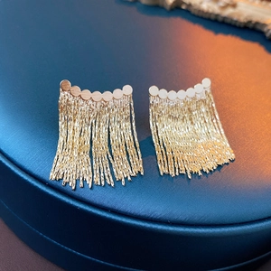 Macro shot of gold tassel earrings with circular chain links on a premium display base