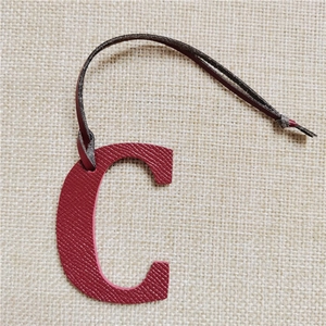 Detail of red textured leather letter C charm with dark brown strap for handbags