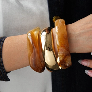 Close-up of layered amber resin bangles and polished gold metal bracelet on a model