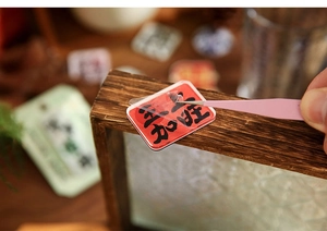 Detail showing hand using tweezers to peel a red Chinese festive sticker onto wood