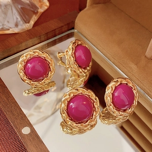 Detail view of vintage gold chain-wrapped earrings with magenta stone on mirror surface