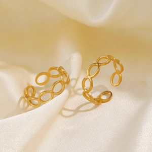 Set of two gold hollow geometric titanium steel rings on warm beige silk background