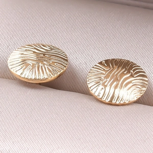 Macro view of gold round earrings with unique ripple texture on beige velvet display