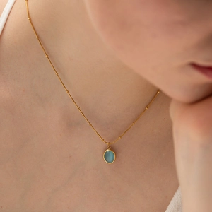 Dettaglio della collana di perle dorate con gemma ovale blu chiaro sul modello