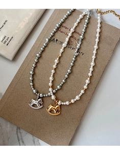 Detail of rocking horse pendant pearl necklaces in gold and silver finishes on a book