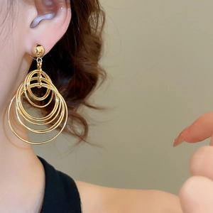 Close-up of a model wearing gold multi-layered geometric hoop earrings in a metal finish