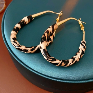 Détail de boucles d'oreilles léopard avec métal doré posées sur un support vert foncé