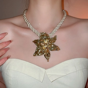 Close-up of a large gold metallic flower pendant with a white braided cord on a model
