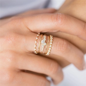 Close-up of four stacked luxury gold rings with sparkling crystals on a model's hand