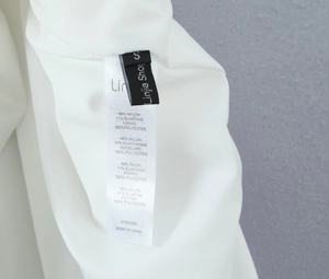 Close-up of white dress garment care label showing 89% nylon and 11% spandex materials