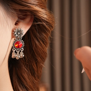 Close-up of vintage silver flower earring with red gemstone and dangling bells on model