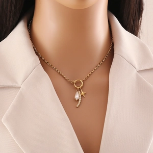 Dettaglio di una collana a cuore dorata con perla, stella e cristalli indossata da una modella