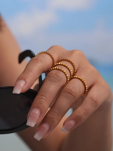 Detail view of gold-plated stainless steel gear rings stacked on finger with sea background