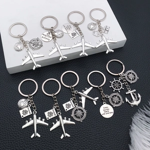 Silver metal travel keychains with airplane, globe and passport charms set on a desk