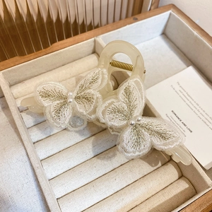 Detail of elegant butterfly embroidery with pearls on cream-colored resin hair claw clip