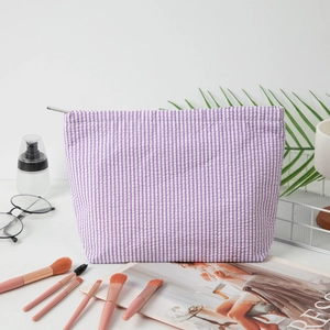 Purple and white seersucker striped cosmetic bag with silver zipper on vanity desk