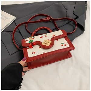 Détail du sac à main avec motif cerises, rabat ondulé et fermoir fleur dorée