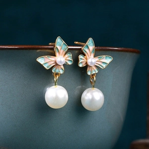 Macro shot of gradient enamel butterfly earrings with hanging white pearls on ceramic