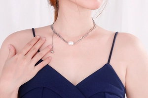Detail of silver asymmetric chain necklace with white pearl and sleek spherical pendant