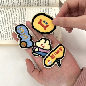 Detail of four cartoon embroidered patches held in hand over an open book background