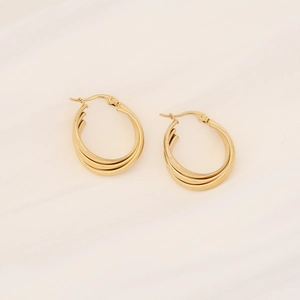 Macro shot of gold multi-layer C-shaped stud earrings on soft silk fabric background