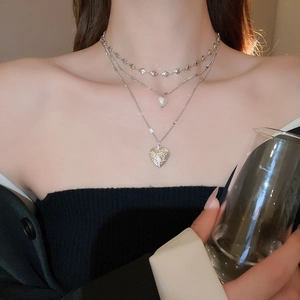 Close-up of triple-layered silver necklace with pearl heart and embossed locket pendant