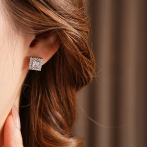Macro shot of silver square zircon stud earrings worn by a model with soft lighting