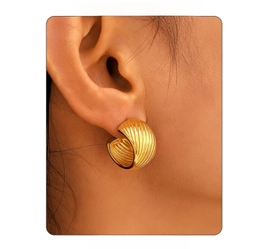 Close-up of a model wearing a gold C-shaped twisted earring with a polished metal texture