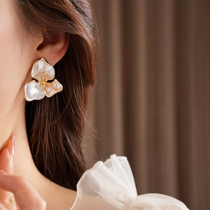 Detailed view of white floral stud earring with gold accents worn by a model