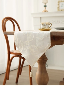 Detail view of cream-colored rectangular table runner with leaf jacquard and elegant tassel