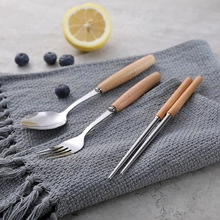 Close-up of stainless steel cutlery set with wooden handles on a gray textile