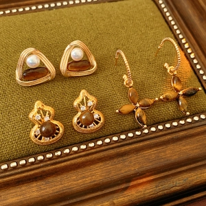 Detailed macro view of vintage gold earrings with tiger eye stones and pearls on dark fabric