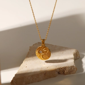 Detail of gold titanium steel sun and moon necklace with zircon on stone display