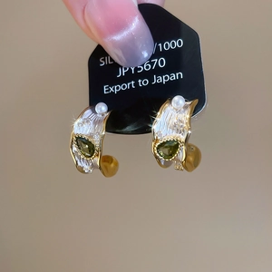 Macro detail of C-shaped earrings featuring green teardrop stones and pearls