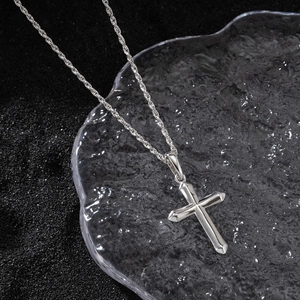 Polished silver cross pendant on a rope chain displayed on a textured water-ripple tray