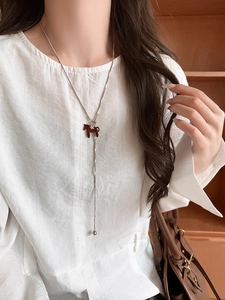 Detail of silver snake chain necklace with red horse pendant and star on white shirt